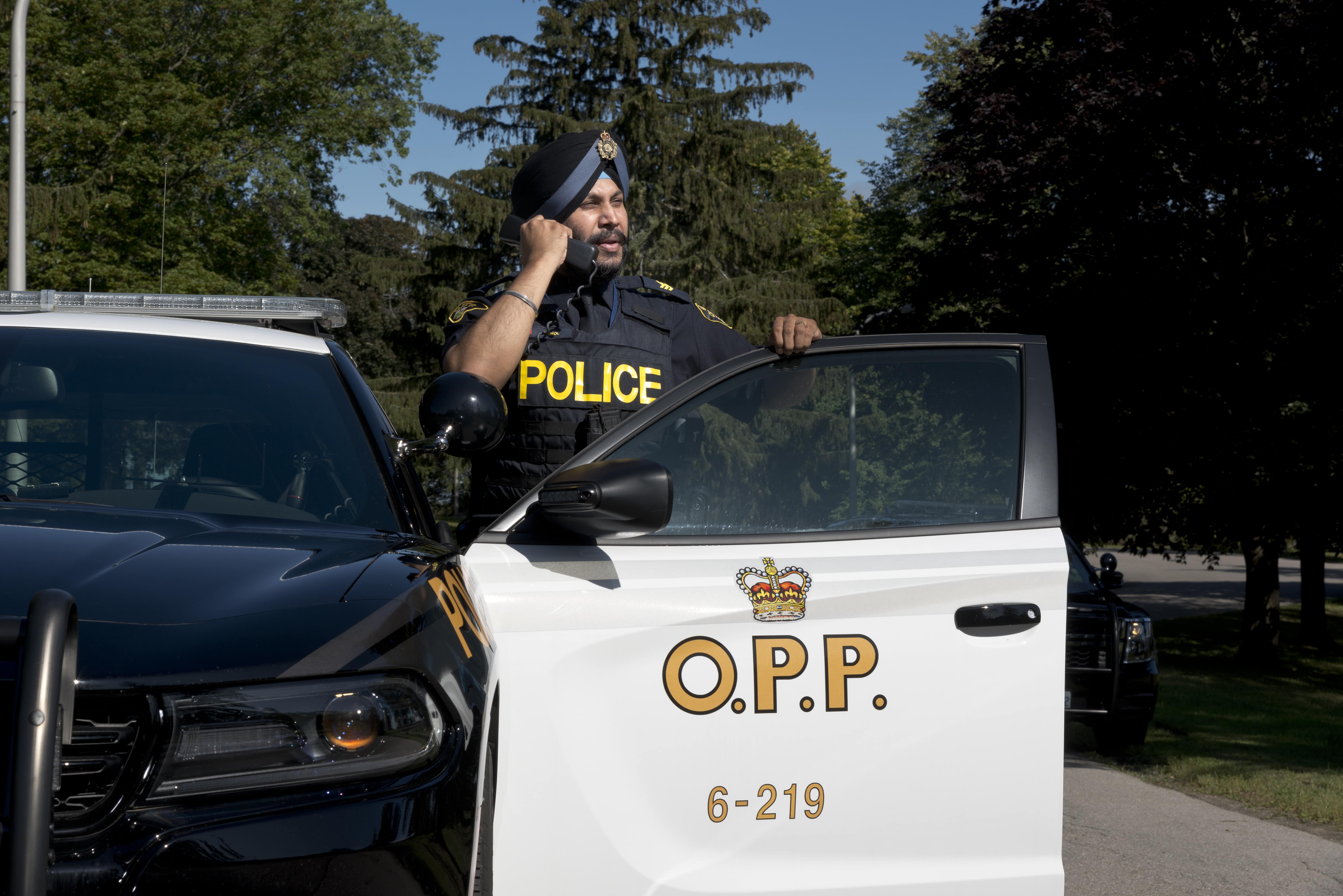 an officer leaning on an OPP cruiser makes a call over the radio