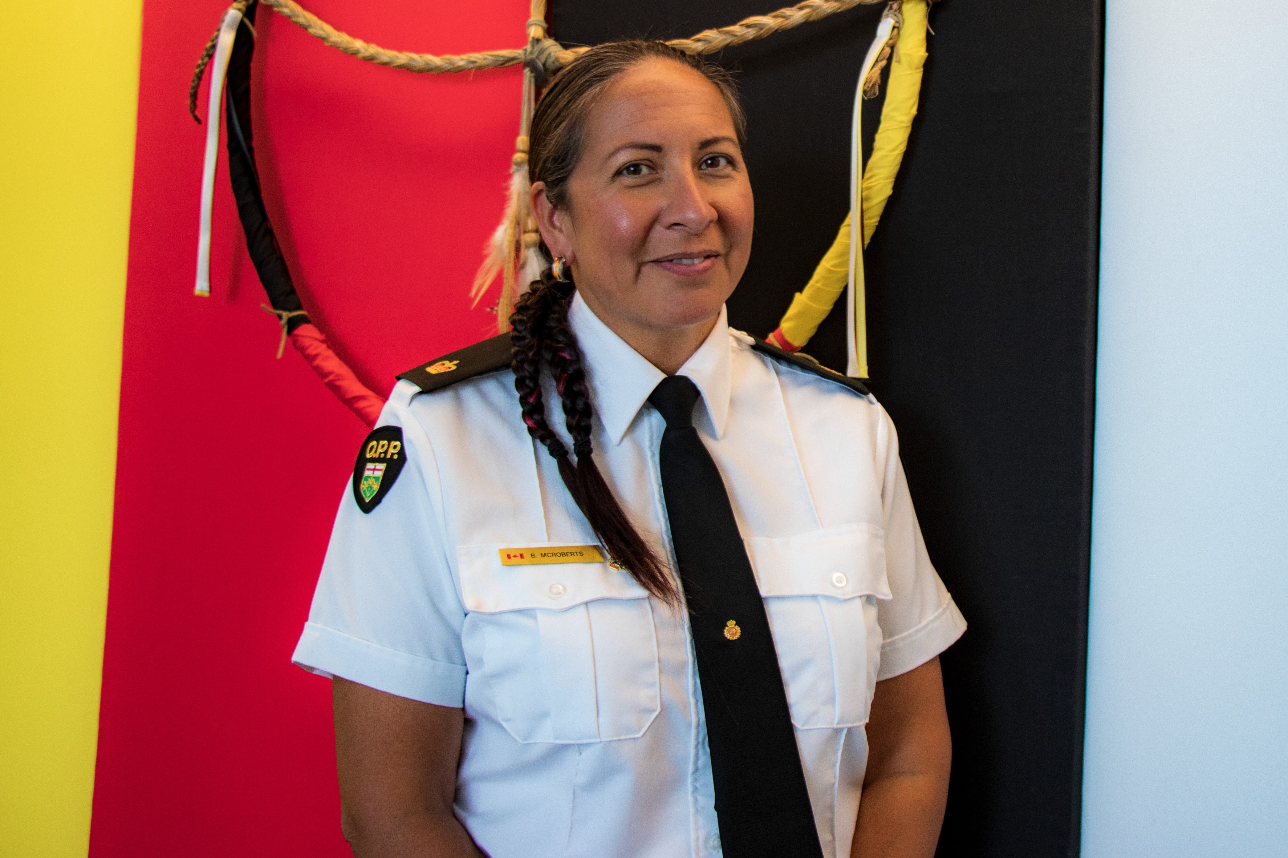 a smiling officer standing in-front of an indigenous flag